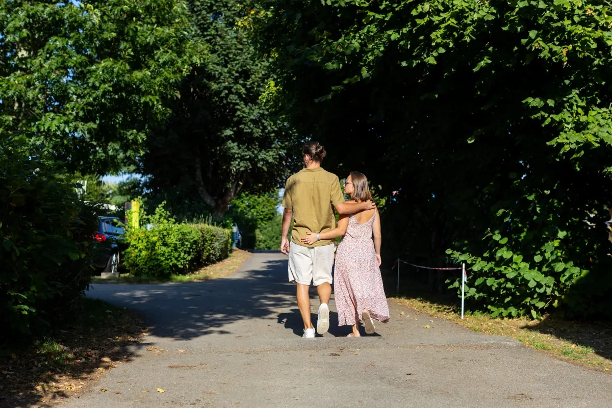 Clément et Manon marchant bras dessus bras dessous dans une allée ombragée de camping